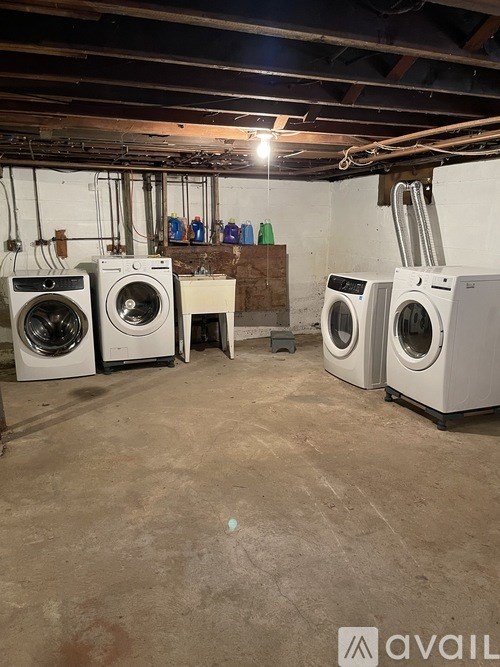 A room with a floor of concrete and a wall of pipes and a washing machine.
