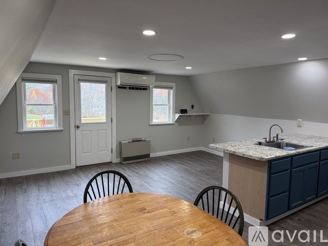 A kitchen with a table and chairs in the foreground and a window with a view of a garden outside.