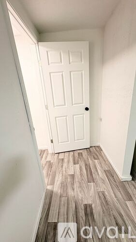 A white door is in a hallway with wood flooring.