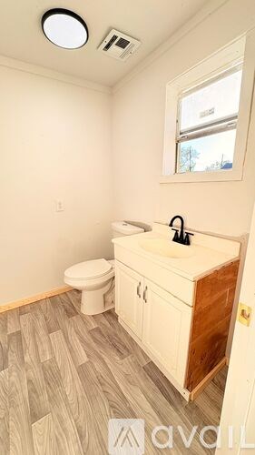 A bathroom with a toilet, sink, and wood cabinet.