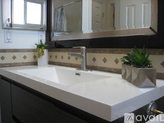 A bathroom sink with a silver faucet and a small plant on the counter.