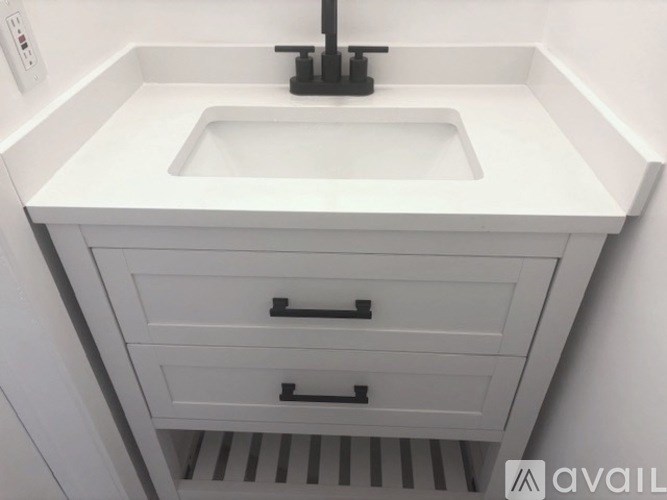 A white bathroom sink with a black faucet and a white cabinet with two drawers.