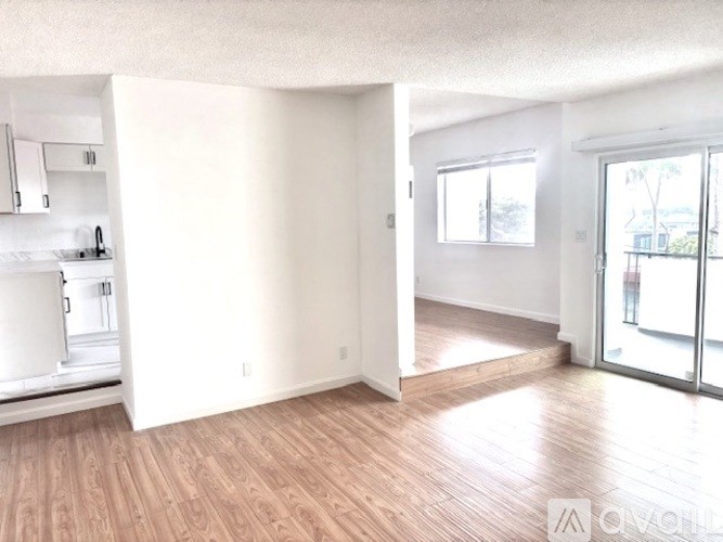 A spacious room with wooden flooring and a sliding glass door leading to a balcony.