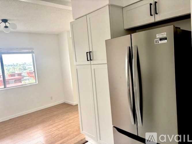 A kitchen with a refrigerator, cabinets, and a window.