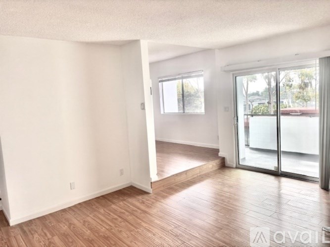 A spacious room with wooden flooring and a sliding glass door leading to a balcony.
