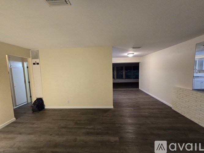 A room with a wooden floor and a white wall with a door and a window.