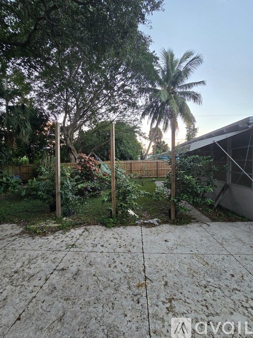 A backyard with a concrete patio, a fence, and a tree.