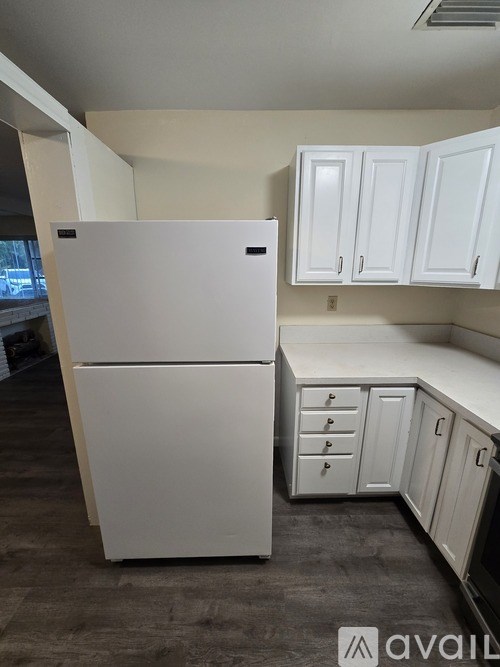 A white refrigerator in a kitchen with white cabinets.