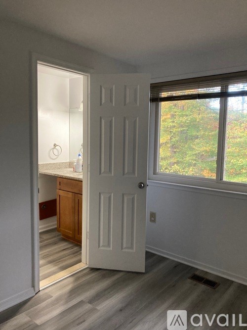 A white door is open to a room with a window and a view of trees outside.
