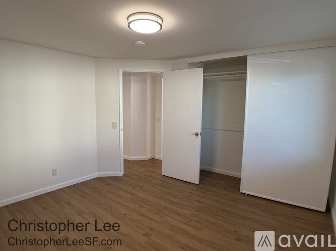 A room with white walls and wooden flooring, with a door on the left and a white cabinet on the right.
