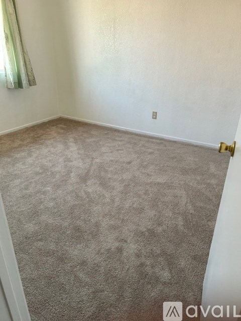 A room with a carpeted floor and a window with a green curtain.