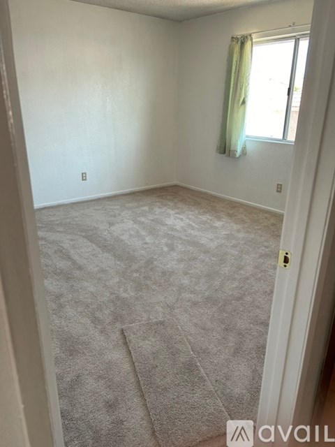 A room with a carpeted floor and a window with a green curtain.