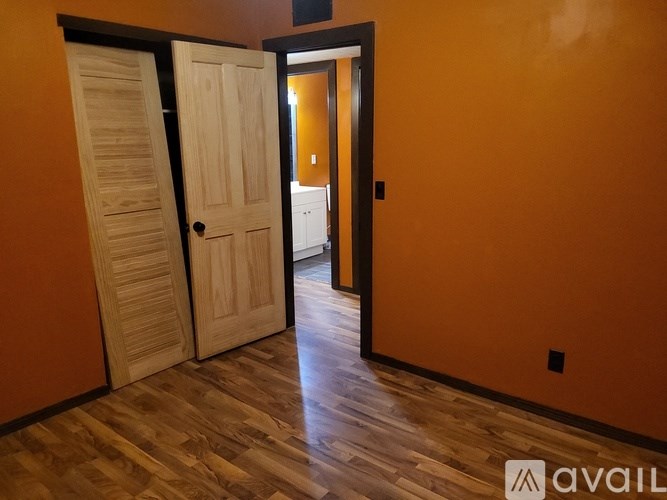 A room with a wooden floor and orange walls with two doors.