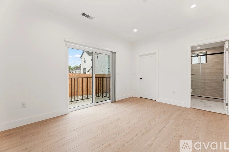 A spacious room with wooden flooring and a sliding glass door leading to a balcony.