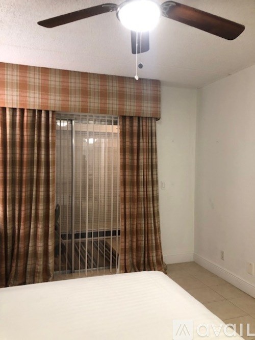 A room with a ceiling fan and a window with a brown curtain.