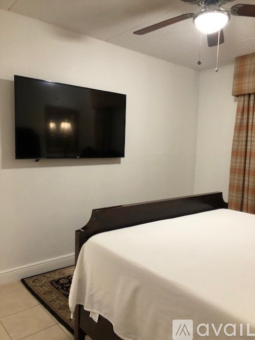 A bedroom with a bed, a television, and a ceiling fan.