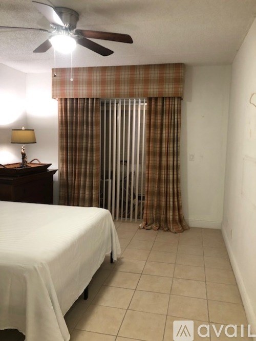 A bedroom with a bed, a ceiling fan, and a window with curtains.