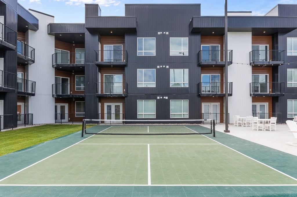 A tennis court in front of a black and white apartment building.