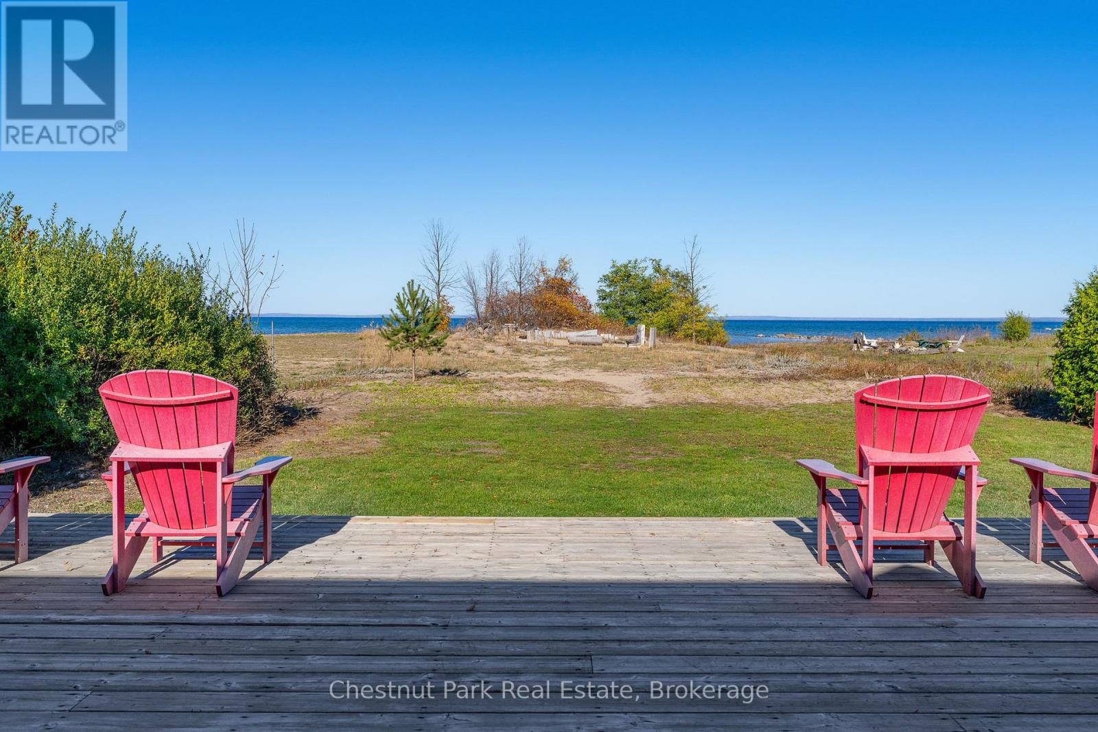 A red chair is on a wooden deck overlooking a grassy area.