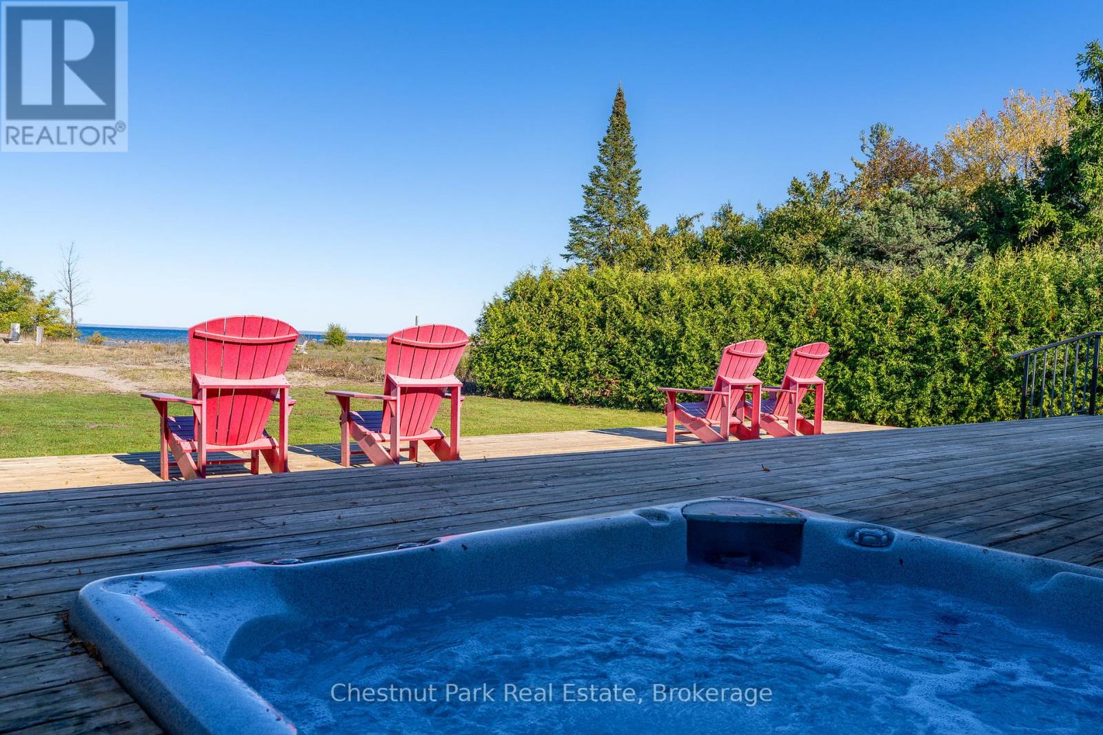 A hot tub sits on a deck with red chairs around it.