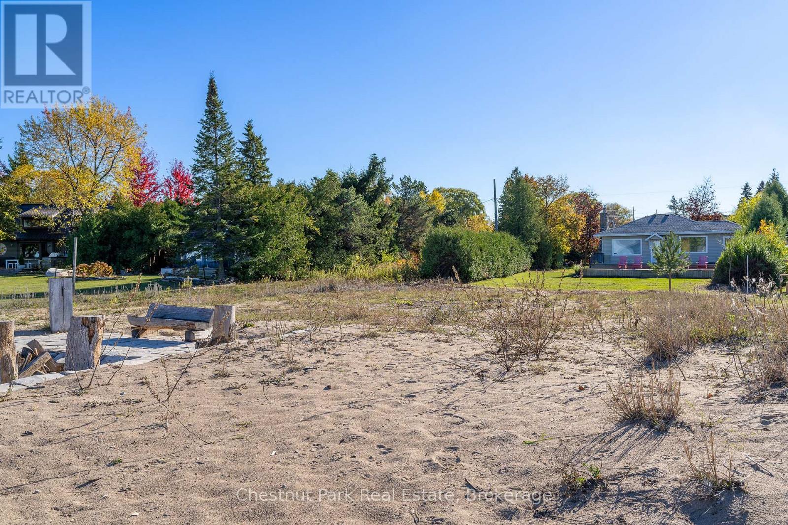 A real estate brokerage logo is superimposed on a photo of a barren field with a bench and trees in the background.