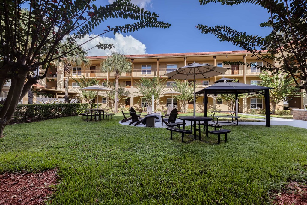 A large building with a balcony overlooks a grassy area with picnic tables and umbrellas.