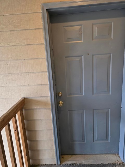 A grey door with a gold handle is set in a white wall.