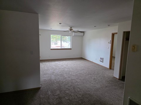 A room with a carpet floor and a window with a fan on the ceiling.