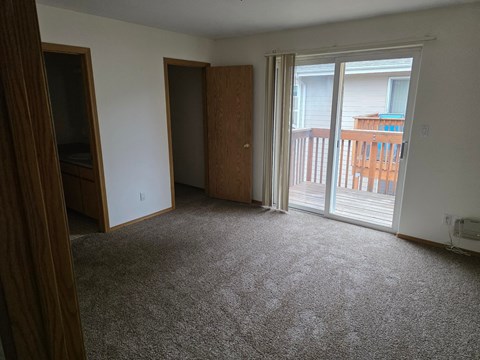 A room with a carpeted floor and a sliding glass door leading to a balcony.