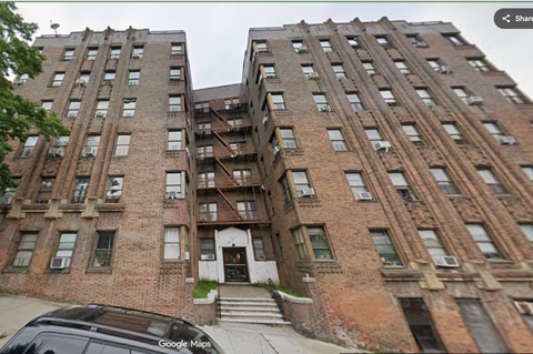 A street view of a large brick building with a car parked in front.