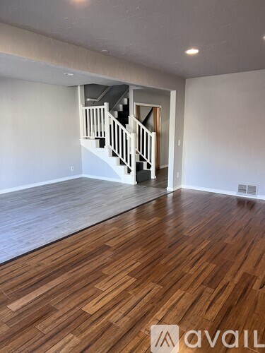 A room with wooden flooring and a staircase in the background.