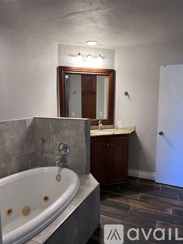 A bathroom with a tub, sink, mirror, and wooden cabinets.