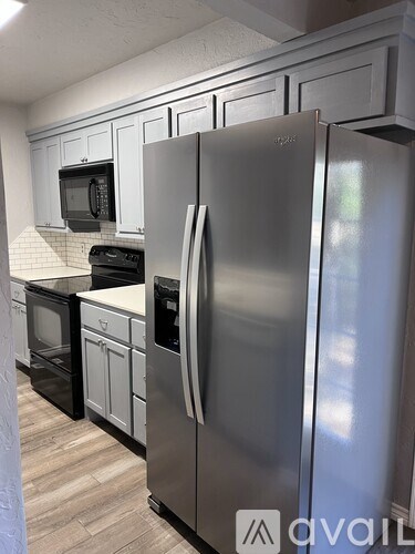 A stainless steel refrigerator stands in a kitchen with white cabinets and black appliances.