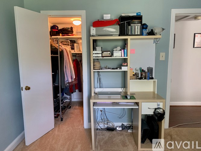 A room with a desk and a closet with clothes.