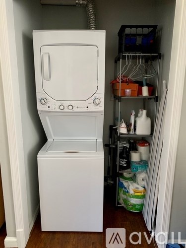 A white washing machine is in a small room with a shelf full of cleaning supplies.
