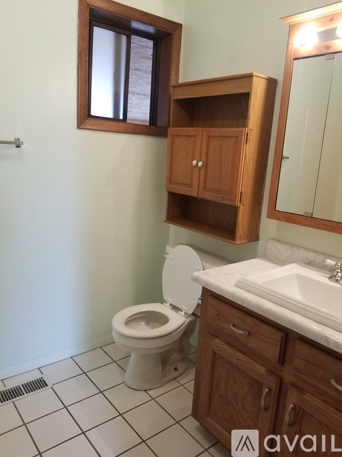 A bathroom with a toilet, sink, and wooden cabinet.