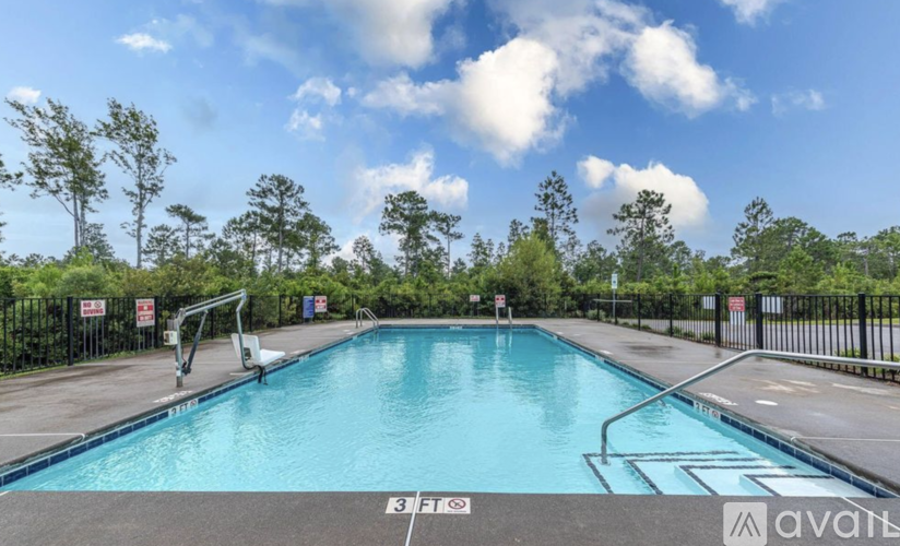 A large outdoor swimming pool surrounded by a fence with trees in the background.