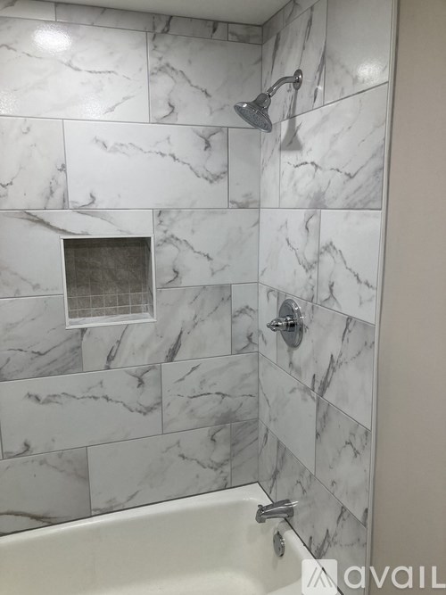 A bathroom with a marble tile wall and a white tub.