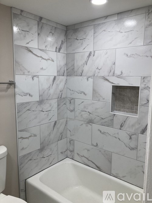 A bathroom with a marble tile wall and a white bathtub.