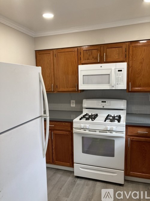 A kitchen with a white refrigerator, white stove, and brown cabinets.