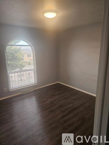 A room with wooden flooring and a window with a view of a building outside.