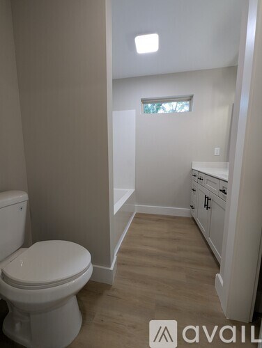 A white toilet in a small bathroom with wooden floors and a window.