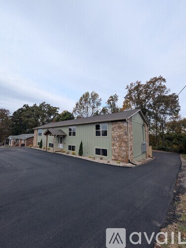 A building with a grey exterior is surrounded by a paved area and trees.