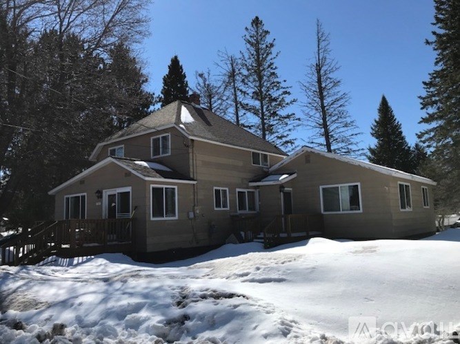 A house with a brown roof and a deck is surrounded by snow.
