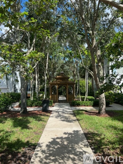 A gazebo is surrounded by trees and a concrete walkway.