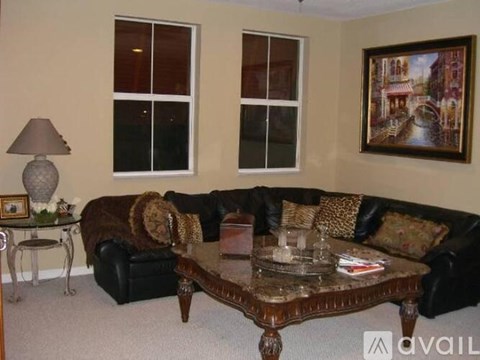 A living room with a black couch, a coffee table, and a painting on the wall.