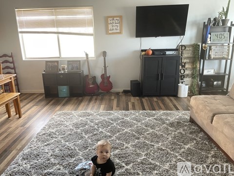 A baby is sitting on a rug in a living room with a guitar and a TV in the background.