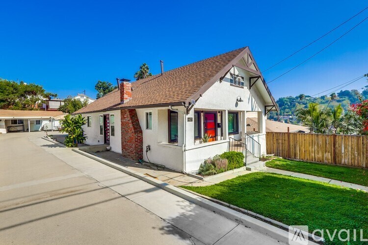 A white house with a brown roof and a red door is surrounded by a wooden fence.