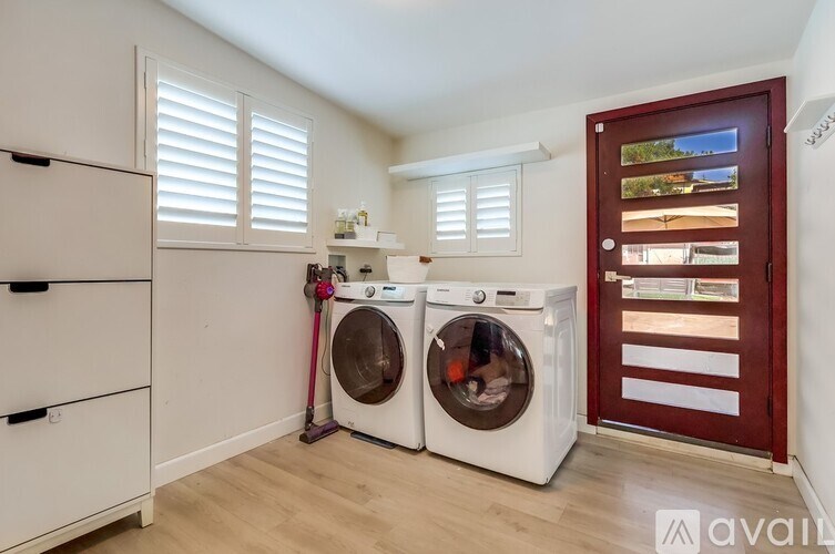 A laundry room with a washer and dryer, a white cabinet, and a red door.