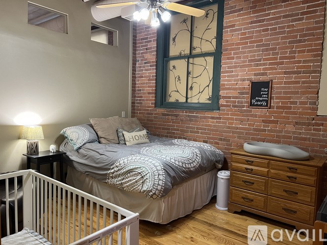 A bedroom with a brick wall and a bed with a grey and white patterned comforter.